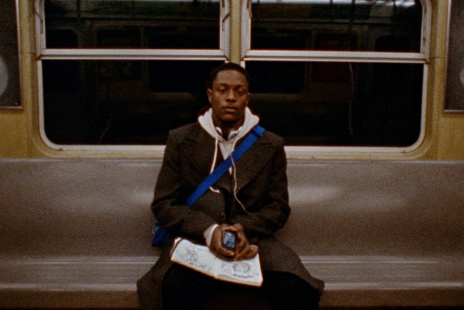 Art student sketching on the train with a phone propped against a cobalt bag strap